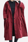 A person is shown wearing the looselyboho Burgundy One Size Fits All Oversized Waterproof Windbreaker Jacket over a black turtleneck. The long, loose-fitting, hooded maroon coat features large front pockets and an unbuttoned top for easy movement. Their hands rest comfortably in the jacket's pockets, offering both style and wind protection.