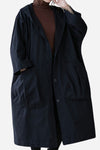 A person is wearing a Black One Size Fits All Oversized Waterproof Windbreaker Jacket from looselyboho. The jacket features large front pockets, offers excellent wind protection, has a button-up front, and falls below the knees. The person is also wearing a brown turtleneck underneath and is depicted from the shoulders to mid-thigh.