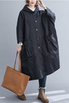 A person is pictured wearing a Black One Size Fits All Oversized Waterproof Windbreaker Jacket from looselyboho. They are also dressed in jeans and brown lace-up boots, and are holding a large brown tote bag in their right hand. The background is plain and light-colored.