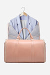 The Smart No-Wrinkle Foldable Travel Bag Pink is displayed in front of The Windbreaker Jacket on a wooden hanger. The jacket, with its arms folded back and interior lining exposed, is partially visible. A plain white background highlights the sleek and practical design of both items.