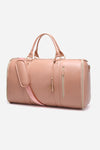 The Smart No-Wrinkle Foldable Travel Bag Pink by The Windbreaker Jacket is crafted from lightweight and portable waterproof PU leather. It comes with two carry handles, a detachable shoulder strap, and features gold zippers along with zippered side pockets adorned with a decorative tassel. This smooth, slightly shiny pink duffel bag is shown against a plain white background.