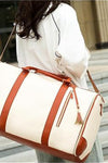 A person with long hair, wearing a white shirt, is carrying a large pink Smart No-Wrinkle Foldable Travel Bag from The Windbreaker Jacket with brown straps and accents. The scene is set outdoors with blurred architectural elements in the background.